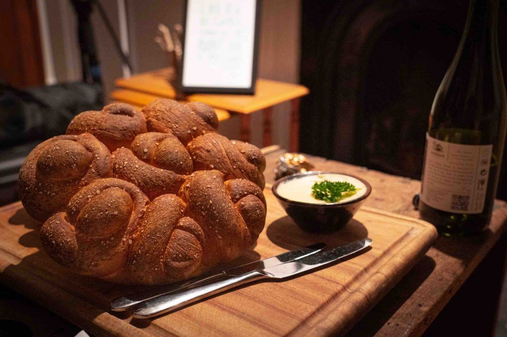 A braided challah on a wooden board beside a bottle of wine, set for Shabbos