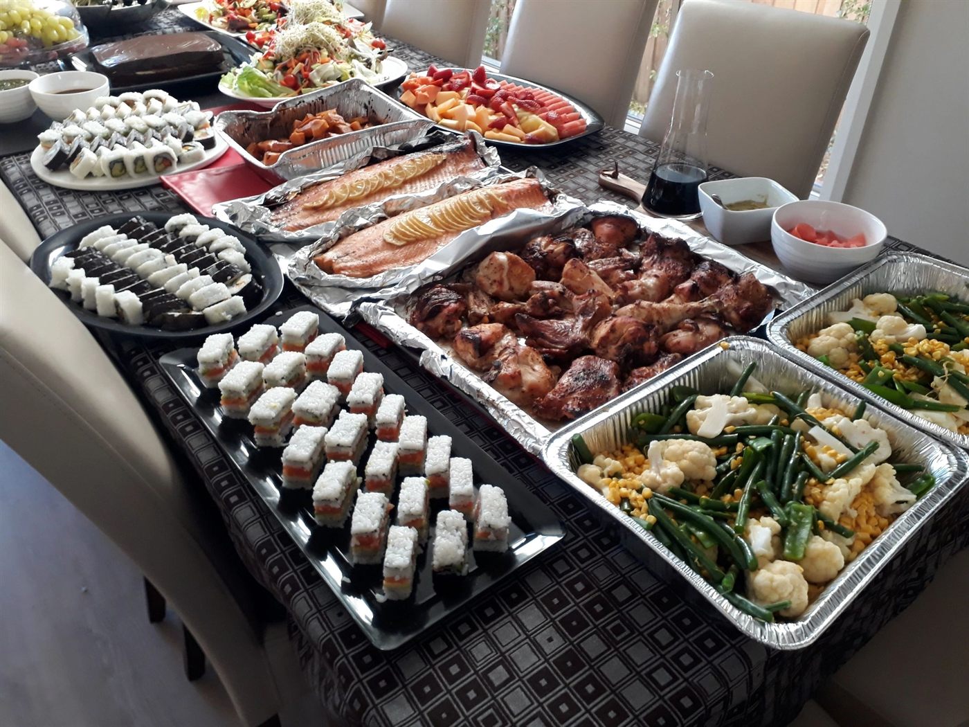 A table set with trays of roast chicken pieces, whole salmon fillets and green beans with cauliflower