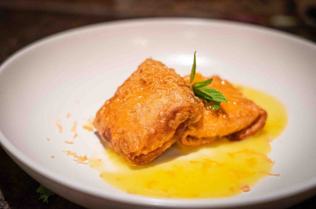 A plated pastry dessert with a warm golden sauce and fresh mint